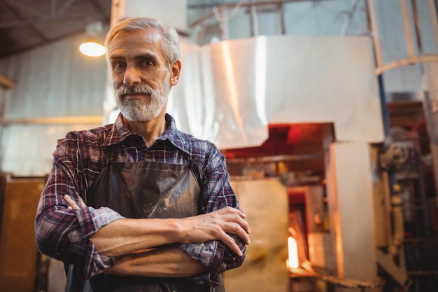 Souffleur de verre debout avec les bras croisés à l'usine de soufflage de verre