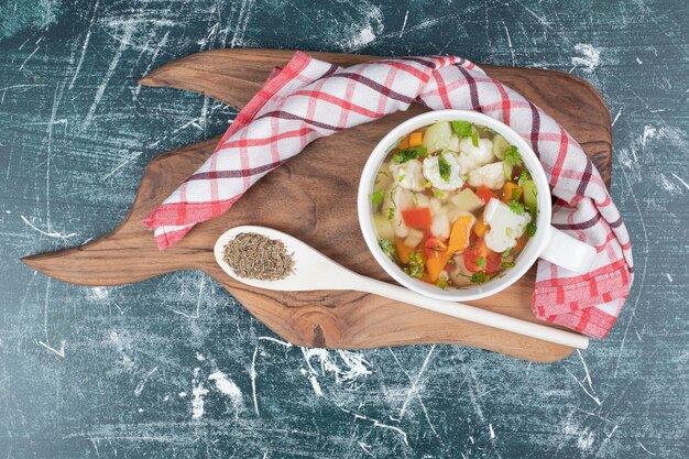 Soupe aux légumes sur planche de bois avec cuillère et nappe.