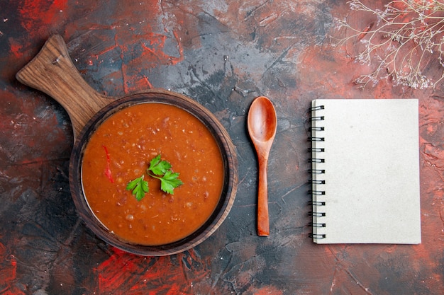 Photo gratuite soupe aux tomates sur une planche à découper brune et ordinateur portable sur une table de couleurs mélangées