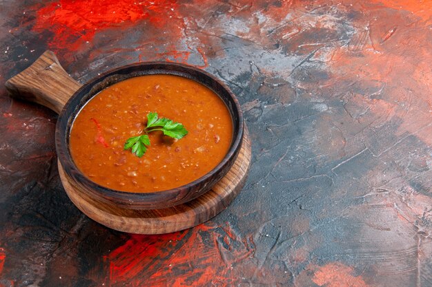 Soupe aux tomates savoureuse sur une planche à découper brune sur le côté droit d'une table de couleurs mélangées