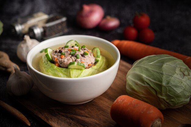 Soupe de chou de porc aux carottes, oignons verts hachés, concombre dans une assiette en bois sur une plaque en bois