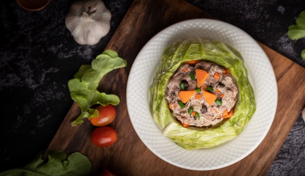 Photo gratuite soupe de chou de porc aux carottes, oignons verts hachés, concombre dans une assiette en bois sur une plaque en bois