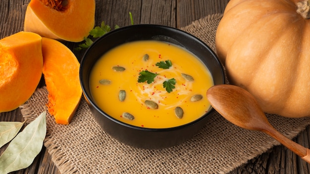 Photo gratuite soupe de citrouille à angle élevé dans un bol avec citrouille et cuillère en bois