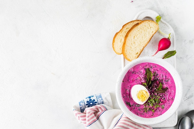 Soupe d'été froide de betteraves, de concombres et d'œufs dans une assiette blanche sur une table en pierre blanche