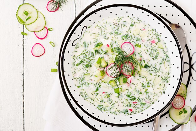 Soupe froide aux concombres frais, radis au yaourt dans un bol sur une table en bois. Cuisine russe traditionnelle - okroshka. Repas végétarien. Vue de dessus. Mise à plat