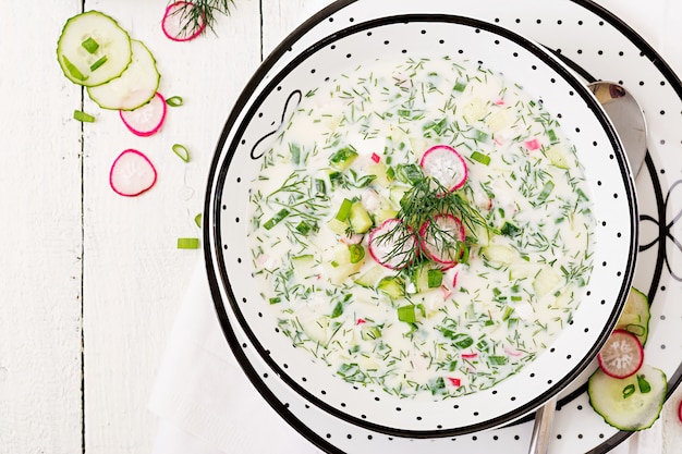 Soupe froide aux concombres frais, radis au yaourt dans un bol sur une table en bois. Cuisine russe traditionnelle - okroshka. Repas végétarien. Vue de dessus. Mise à plat