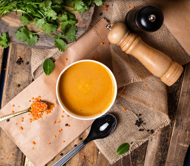 Soupe de lentilles rouges dans un bol en verre jetable servi avec des légumes verts.