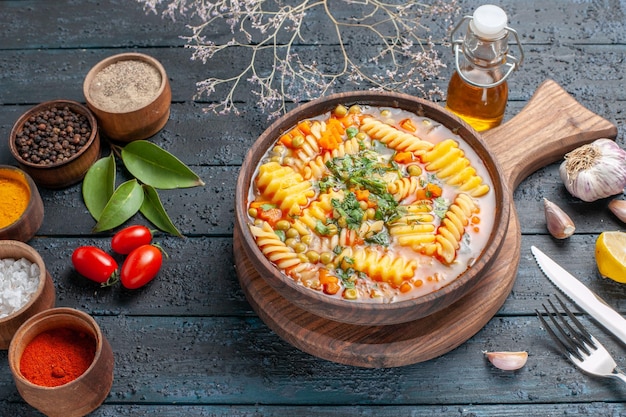 Soupe de pâtes délicieuse vue à mi-hauteur de pâtes italiennes en spirale avec assaisonnements sur un bureau bleu foncé soupe de pâtes plat de couleur dîner cuisine