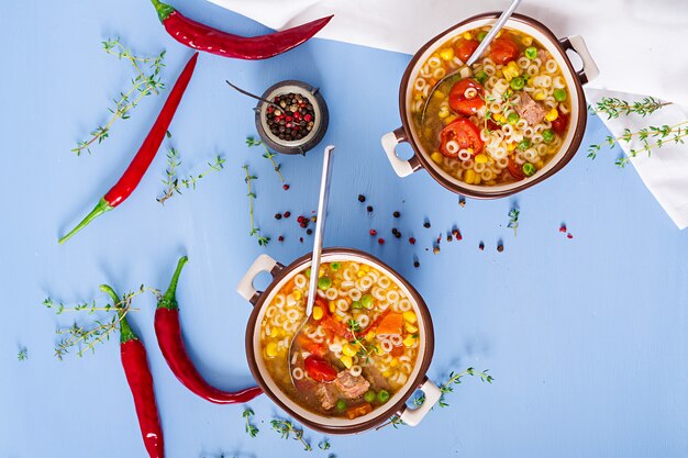 Soupe avec de petites pâtes, des légumes et des morceaux de viande dans un bol sur une table bleue. Nourriture italienne.