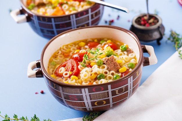 Soupe avec de petites pâtes, des légumes et des morceaux de viande dans un bol sur une table bleue. Nourriture italienne.
