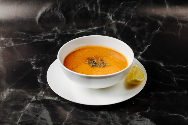 Soupe de potiron dans un bol blanc avec des herbes et des épices, avec une tranche de citron autour.