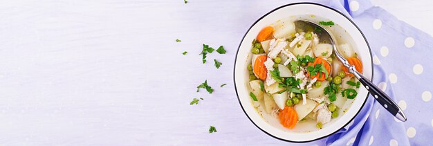 Soupe de poulet aux petits pois, carottes et pommes de terre dans un bol blanc