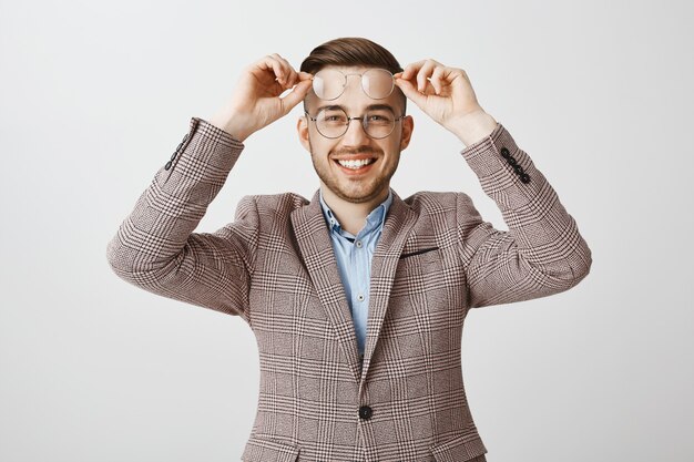 Souriant beau mec en costume essayant de nouvelles lunettes, choisissant des lunettes