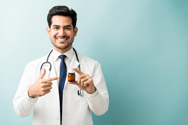 Souriant beau médecin montrant une bouteille de médicament sur fond bleu