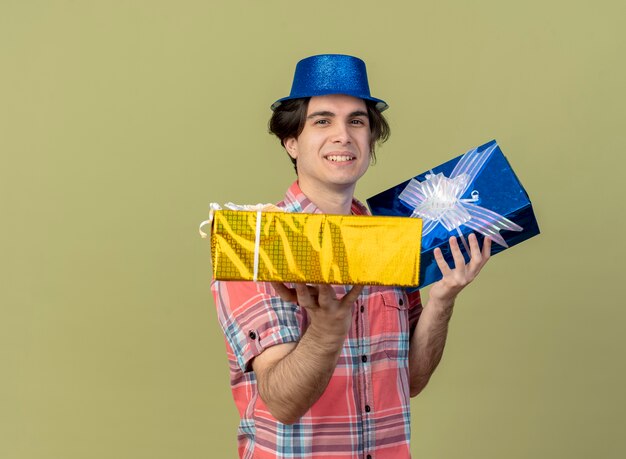 Souriant bel homme caucasien portant un chapeau de fête bleu détient des coffrets cadeaux