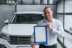 Photo gratuite souriant et de bonne humeur. manager se tient devant une voiture blanche moderne avec du papier et des documents en mains
