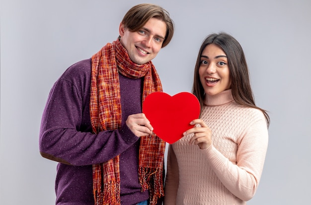 Souriant à la caméra jeune couple le jour de la Saint-Valentin tenant une boîte en forme de coeur isolé sur fond blanc
