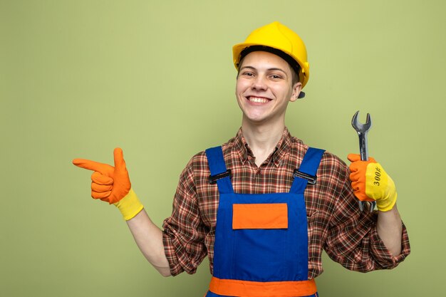 Souriant à côté d'un jeune constructeur masculin en uniforme avec des gants tenant une clé à fourche