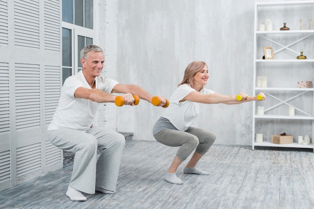 Souriant couple aîné effectuant des exercices avec des haltères à la maison