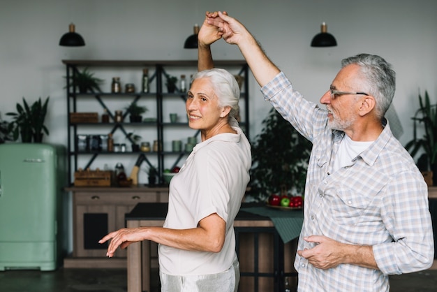 Souriant couple de personnes âgées dansant ensemble dans la cuisine