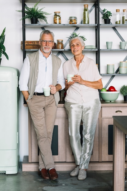 Souriant couple de personnes âgées debout devant l&#39;étagère, tenant une tasse de café