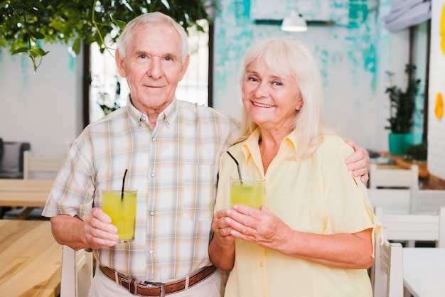 Souriant embrassant couple de personnes âgées tenant des verres de jus