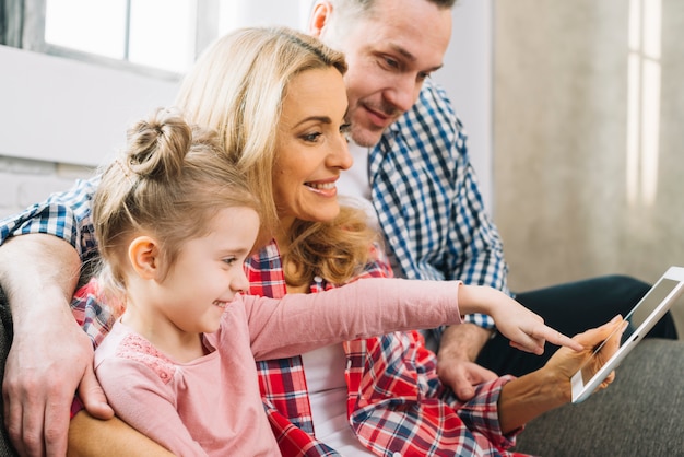 Photo gratuite souriant famille en regardant une vidéo tandis que sa fille pointant sur une tablette numérique