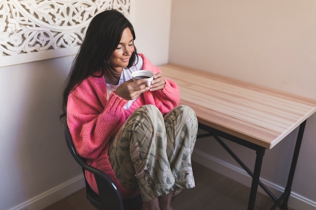 Souriant fille assise sur une chaise tenant profitant de boire du café