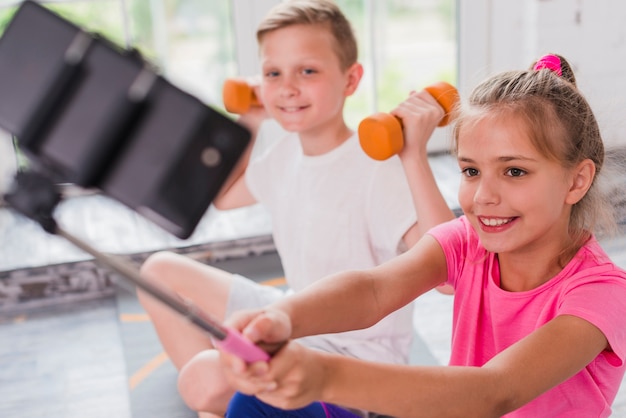 Souriant fille prenant selfie sur téléphone portable assis avec son ami exerçant avec des haltères