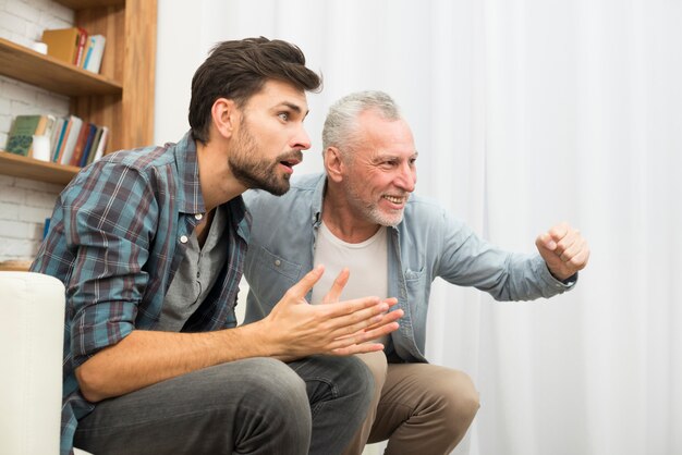 Souriant homme âgé et concentré jeune homme regardant la télévision sur un canapé