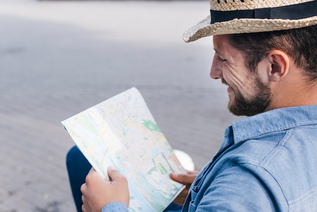 Souriant homme barbu portant chapeau lecture carte à l'extérieur