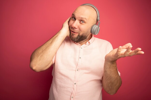 Souriant homme chauve d'âge moyen portant un t-shirt rose et un casque diffusant la main