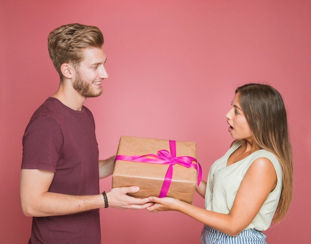 Souriant homme donnant une boîte cadeau à sa copine choquée sur fond coloré