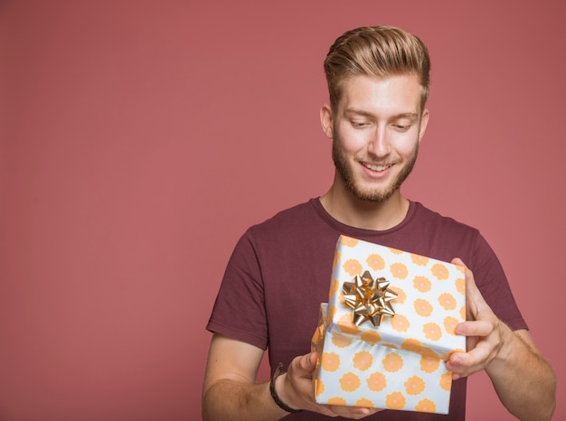 Souriant homme ouvrant boîte-cadeau floral avec archet doré