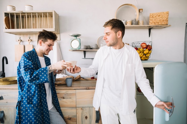 Souriant homme prenant le bol de son ami dans la cuisine