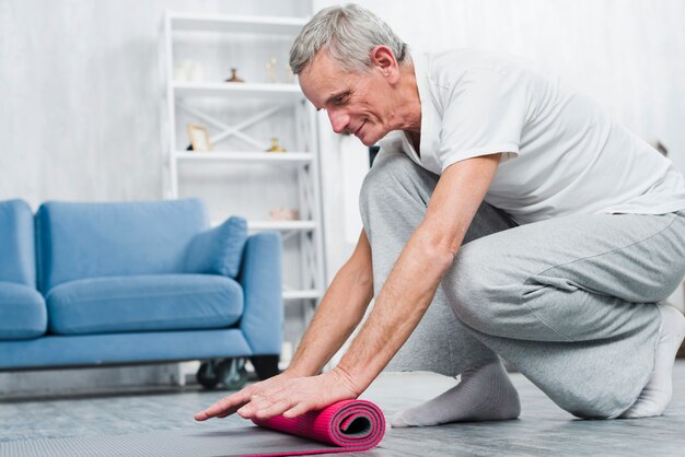 Souriant homme roulant tapis de yoga après le yoga à la maison