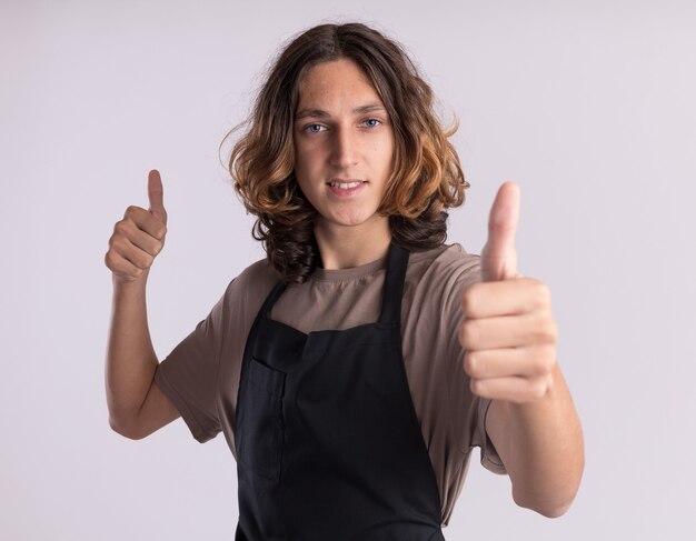 Souriant jeune beau barbier en uniforme montrant les pouces vers le haut