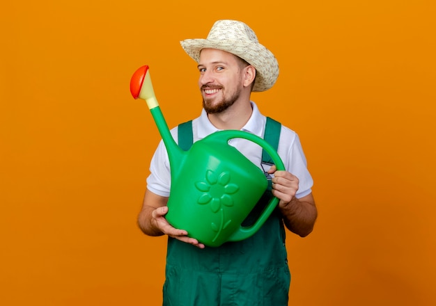 Souriant jeune beau jardinier slave en uniforme et chapeau tenant un arrosoir à la recherche d'isolement