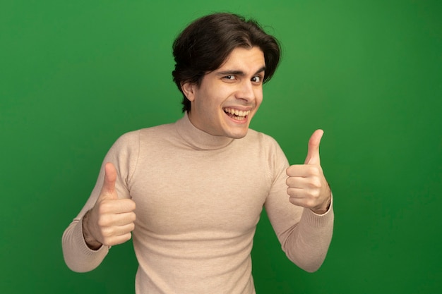 Souriant jeune beau mec montrant les pouces vers le haut isolé sur le mur vert