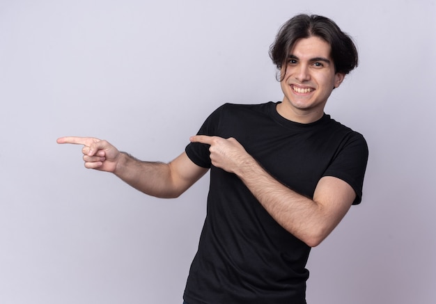 Souriant jeune beau mec portant des points de t-shirt noir sur le côté isolé sur un mur blanc avec espace de copie