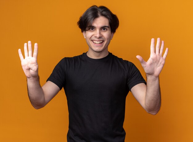 Souriant jeune beau mec portant un t-shirt noir montrant différents numéros isolés sur un mur orange