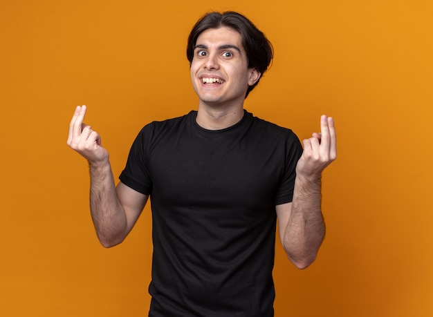 Souriant jeune beau mec portant un t-shirt noir montrant un geste de pointe isolé sur un mur orange