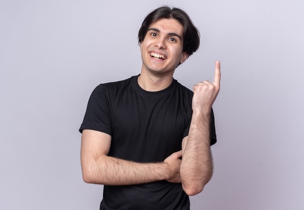 Souriant jeune beau mec portant un t-shirt noir montrant un isolé sur un mur blanc