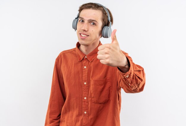 Souriant jeune beau mec vêtu d'une chemise rouge avec des écouteurs montrant le pouce vers le haut