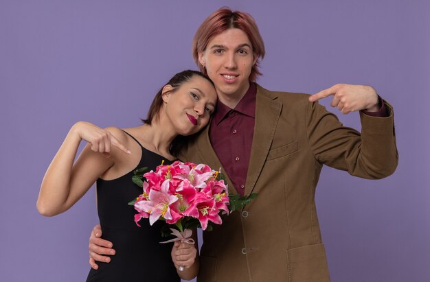 Souriant jeune bel homme et ravie jolie jeune femme pointant sur un bouquet de fleurs