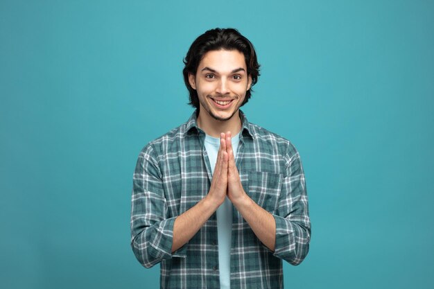 souriant jeune bel homme regardant la caméra montrant le geste de namaste isolé sur fond bleu