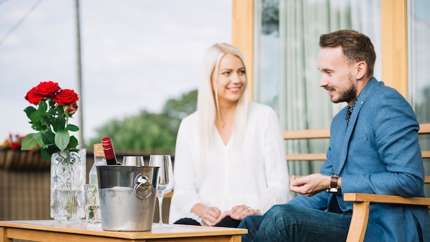 Photo gratuite souriant jeune couple assis avec un seau à glace sur la table