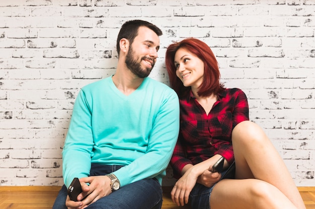 Souriant jeune couple assis avec smartphone