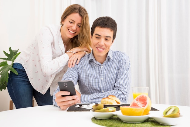 Souriant jeune couple cherche un téléphone portable à la table du petit déjeuner