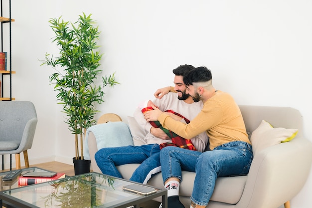 Souriant jeune couple gay assis sur un canapé aimer leur bébé